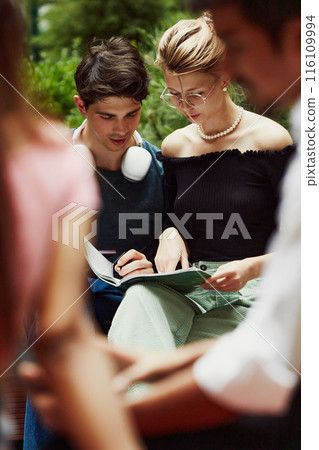 Focused young boy and girl, students sitting outdoors and preparing for lessons, captured involved in common learning Focused young boy and girl, students sitting outdoors and preparing for lessons, captured involved in common learning 116109994