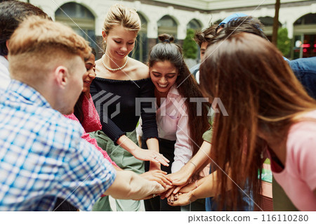 Multiracial people, men and women, students holding hands and showing readiness for common work. Outdoor gathering and studying Multiracial people, men and women, students holding hands and showing readiness for common work. Outdoor gathering and studying 116110280