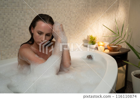 A woman relaxes in a bubble bath surrounded by candles and plants. The atmosphere of psychological problems experienced by a woman A woman relaxes in a bubble bath surrounded by candles and plants. The atmosphere of psychological problems experienced by a woman 116110874