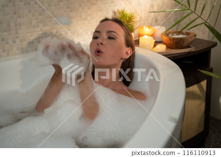 A woman is enjoying a relaxing bath with bubbles and candles. She is in a calm and peaceful state, and the warm light creates a cozy and inviting atmosphere. A woman is enjoying a relaxing bath with bubbles and candles. She is in a calm and peaceful state, and the warm light creates a cozy and inviting atmosphere. 116110913