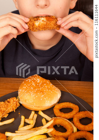 Caucasian man eating fried chicken wings, potato chips, onion rings and chicken wings by hand from a gray plate on a wooden table Caucasian man eating fried chicken wings, potato chips, onion rings and chicken wings by hand from a gray plate on a wooden table 116111644