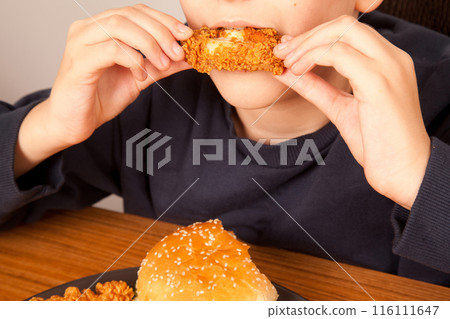 Caucasian man eating fried chicken wings, potato chips, onion rings and chicken wings by hand from a gray plate on a wooden table Caucasian man eating fried chicken wings, potato chips, onion rings and chicken wings by hand from a gray plate on a wooden table 116111647