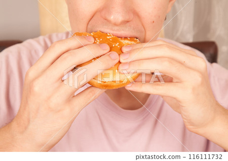 Caucasian young man eats half-eaten sesame fresh hamburger Caucasian young man eats half-eaten sesame fresh hamburger 116111732
