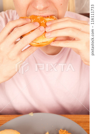 Caucasian young man eats half-eaten sesame fresh hamburger 116111733