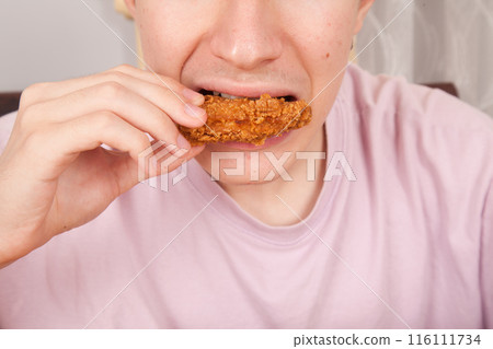 Caucasian man eating fried chicken wings, American fast food culture, cooked chicken pieces Caucasian man eating fried chicken wings, American fast food culture, cooked chicken pieces 116111734