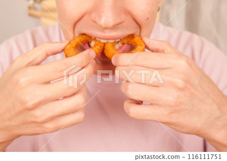 Caucasian man eats fresh fried onion rings with his hands, American fast food culture 116111751