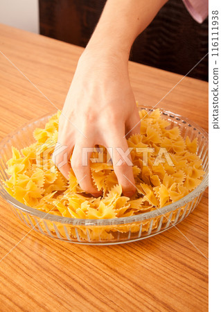 Uncooked raw healthy and pasta macaroni hand held by a Caucasian man, on wooden table in glass plate Uncooked raw healthy and pasta macaroni hand held by a Caucasian man, on wooden table in glass plate 116111938