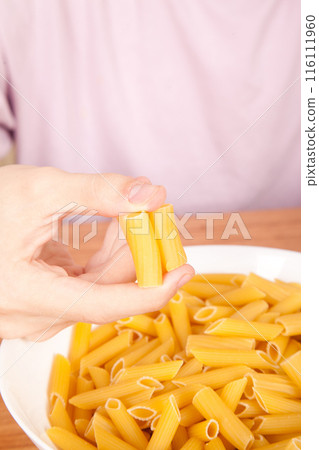 Uncooked raw healthy and pasta macaroni hand held by a Caucasian man, on wooden table in porcelain plate Uncooked raw healthy and pasta macaroni hand held by a Caucasian man, on wooden table in porcelain plate 116111960