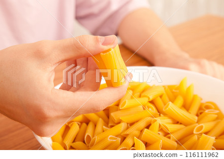 Uncooked raw healthy and pasta macaroni hand held by a Caucasian man, on wooden table in porcelain plate Uncooked raw healthy and pasta macaroni hand held by a Caucasian man, on wooden table in porcelain plate 116111962