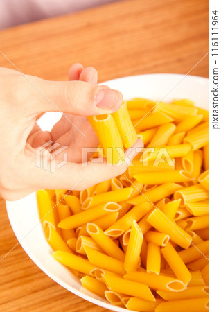 Uncooked raw healthy and pasta macaroni hand held by a Caucasian man, on wooden table in porcelain plate Uncooked raw healthy and pasta macaroni hand held by a Caucasian man, on wooden table in porcelain plate 116111964