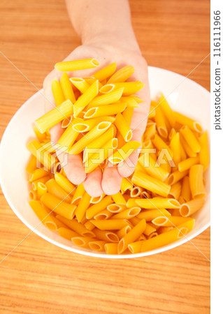Uncooked raw healthy and pasta macaroni hand held by a Caucasian man, on wooden table in porcelain plate Uncooked raw healthy and pasta macaroni hand held by a Caucasian man, on wooden table in porcelain plate 116111966