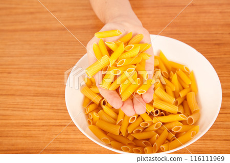 Uncooked raw healthy and pasta macaroni hand held by a Caucasian man, on wooden table in porcelain plate Uncooked raw healthy and pasta macaroni hand held by a Caucasian man, on wooden table in porcelain plate 116111969