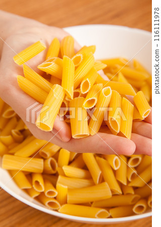 Uncooked raw healthy and pasta macaroni hand held by a Caucasian man, on wooden table in porcelain plate 116111978