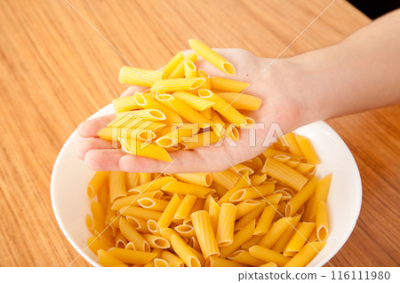 Uncooked raw healthy and pasta macaroni hand held by a Caucasian man, on wooden table in porcelain plate 116111980