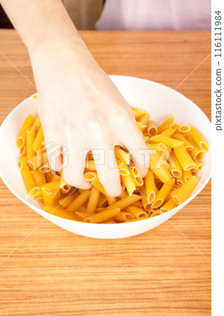 Uncooked raw healthy and pasta macaroni hand held by a Caucasian man, on wooden table in porcelain plate 116111984