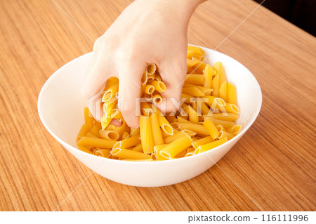 Uncooked raw healthy and pasta macaroni hand held by a Caucasian man, on wooden table in porcelain plate 116111996