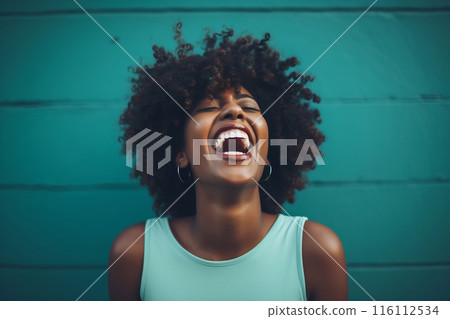 Woman with curly hair laughing against teal wall 116112534