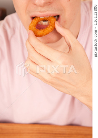 Caucasian man eats fresh fried onion rings with his hands, American fast food culture 116112806