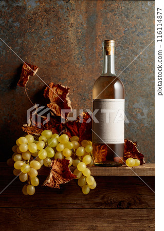 Bottle of white wine with grapes and dried up vine leaves. 116114877