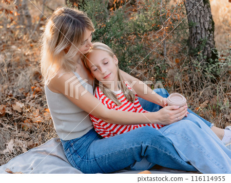 Mother sitting on plaid with her beautiful daughter outdoor in forest with sunshine. Mother sitting on plaid with her beautiful daughter outdoor in forest with sunshine. 116114955