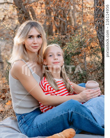 Mother sitting on plaid with her beautiful daughter outdoor in forest with sunshine. Mother sitting on plaid with her beautiful daughter outdoor in forest with sunshine. 116114956