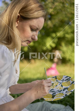 a beautiful young artist in a white dress paints a picture on the river bank a beautiful young artist in a white dress paints a picture on the river bank 116115051