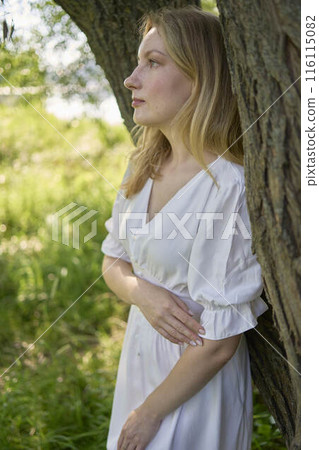 beautiful young artist in a white dress among the trees on the river bank beautiful young artist in a white dress among the trees on the river bank 116115082