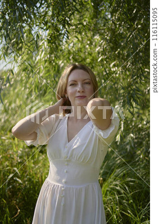 beautiful young artist in a white dress among the trees on the river bank 116115095