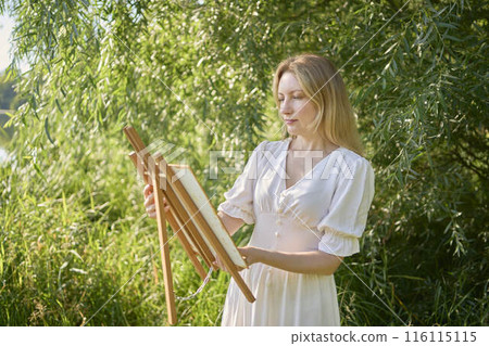 beautiful young artist in a white dress among the trees on the river bank beautiful young artist in a white dress among the trees on the river bank 116115115