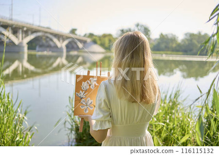 beautiful young artist in a white dress among the trees on the river bank 116115132