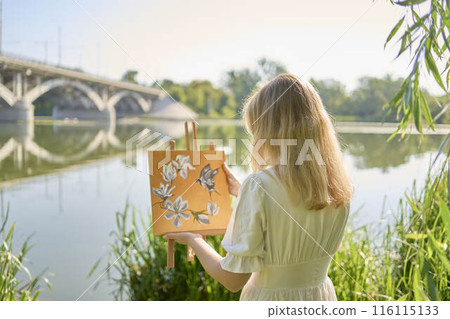 beautiful young artist in a white dress among the trees on the river bank 116115133