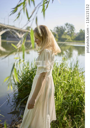 beautiful young artist in a white dress among the trees on the river bank 116115152