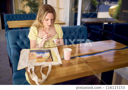 a beautiful young artist in a yellow dress paints a customized shopping bag 116115153