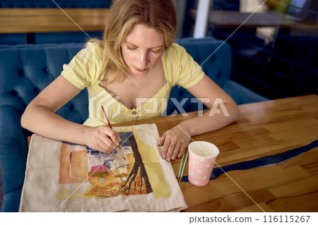 a beautiful young artist in a yellow dress paints a customized shopping bag a beautiful young artist in a yellow dress paints a customized shopping bag 116115267