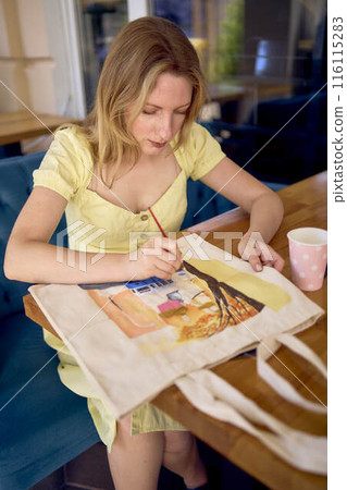 a beautiful young artist in a yellow dress paints a customized shopping bag a beautiful young artist in a yellow dress paints a customized shopping bag 116115283