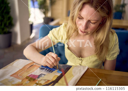a beautiful young artist in a yellow dress paints a customized shopping bag 116115305