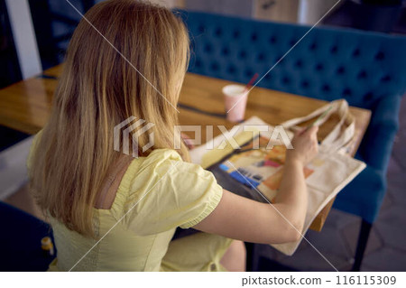 a beautiful young artist in a yellow dress paints a customized shopping bag 116115309