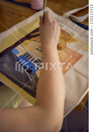 a beautiful young artist in a yellow dress paints a customized shopping bag a beautiful young artist in a yellow dress paints a customized shopping bag 116115313