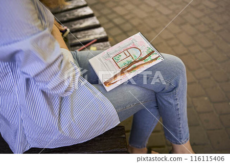 a young artist draws a sketch of a window on the streets of the city 116115406
