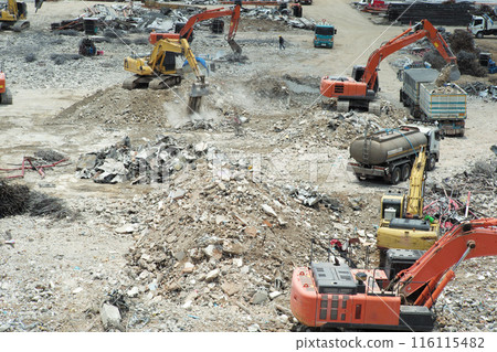 Many excavators working on the ground of the construction site while removing the salvage after the destruction of the building Many excavators working on the ground of the construction site while removing the salvage after the destruction of the building 116115482