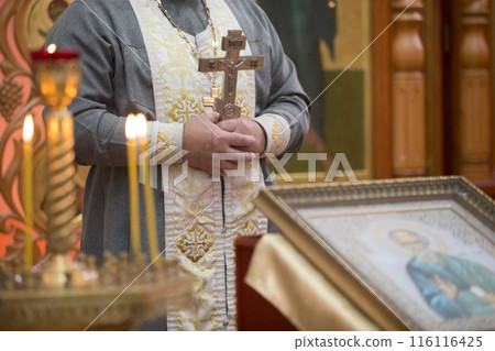 Priest's hand with a cross on the background of church candles. 116116425