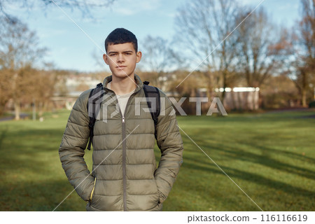 Youthful Elegance: Beautiful 17-Year-Old Boy Standing in the Autumn Park with Lush Green Lawn 116116619