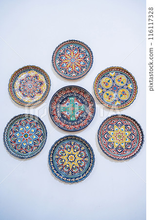 traditional Uzbek ceramic plates hand-painted on white wall at oriental souvenir tableware shop in Uzbekistan 116117328