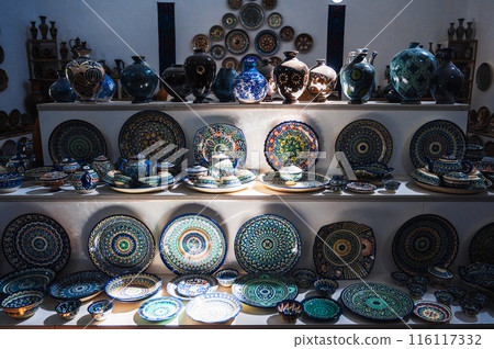 Uzbek handmade ceramic plates and vases with hand-painted traditional Asian patterns on shelves in oriental tableware store 116117332