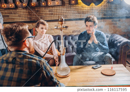 A young pensive company of people is smoking a hookah A young pensive company of people is smoking a hookah 116117595
