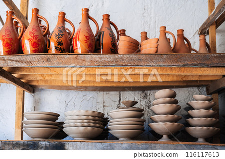 Clay plates and hand-painted Uzbek ceramic jugs on shelf in a pottery workshop in Uzbekistan 116117613