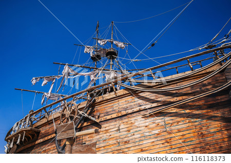 mast with sails on an ancient wooden pirate ship boat on background of blue sky in sea 116118373