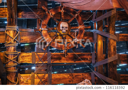 wooden steering wheel with a skull in captain's cabin on an medieval pirate ship 116118392