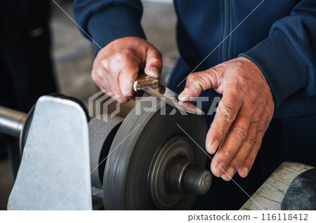 hands of grinder male sharpener sharpening a knife blade on a grinding machine with abrasive wheel in the workshop close-up hands of grinder male sharpener sharpening a knife blade on a grinding machine with abrasive wheel in the workshop close-up 116118412