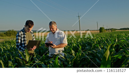 Two farmers working in a field, using a laptop and a tablet. Technology in agriculture Two farmers working in a field, using a laptop and a tablet. Technology in agriculture 116118527